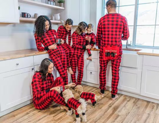 family and two small dogs wearing matching buffalo plaid onesie pajamas interacting with one another in their kitchen