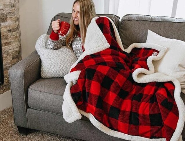 woman laying under Buffalo Plaid Sherpa Blanket on couch holding a mug