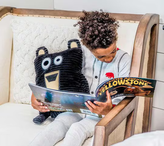 child wearing pajamas sitting in chair reading a book about critters