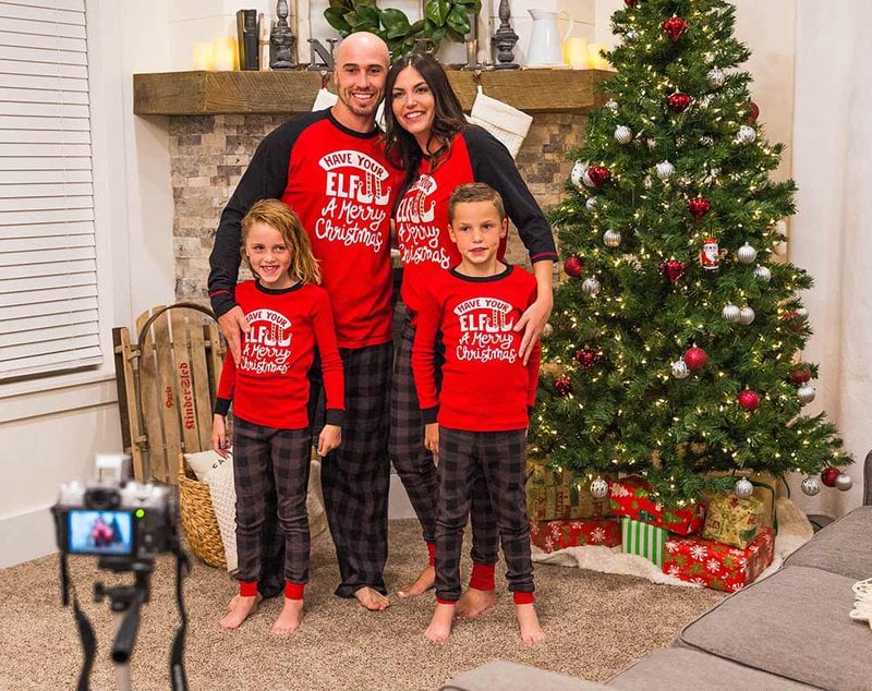 family of four wearing matching Christmas pajamas taking a photo while standing next to a Christmas tree in a cozy living room