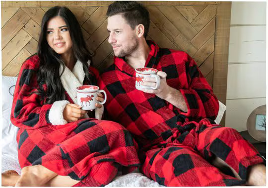couple wearing matching plaid pajamas, laying together drinking from a mug
