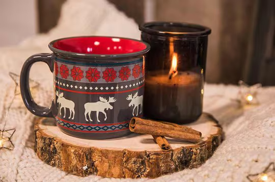 Fair Isle Moose Mug next to a lit candle and cinnamon sticks
