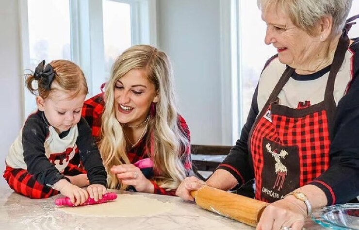 child, mother, grandmother working with dough on kitchen counter wearing plaid moose family matching apron and pajamas