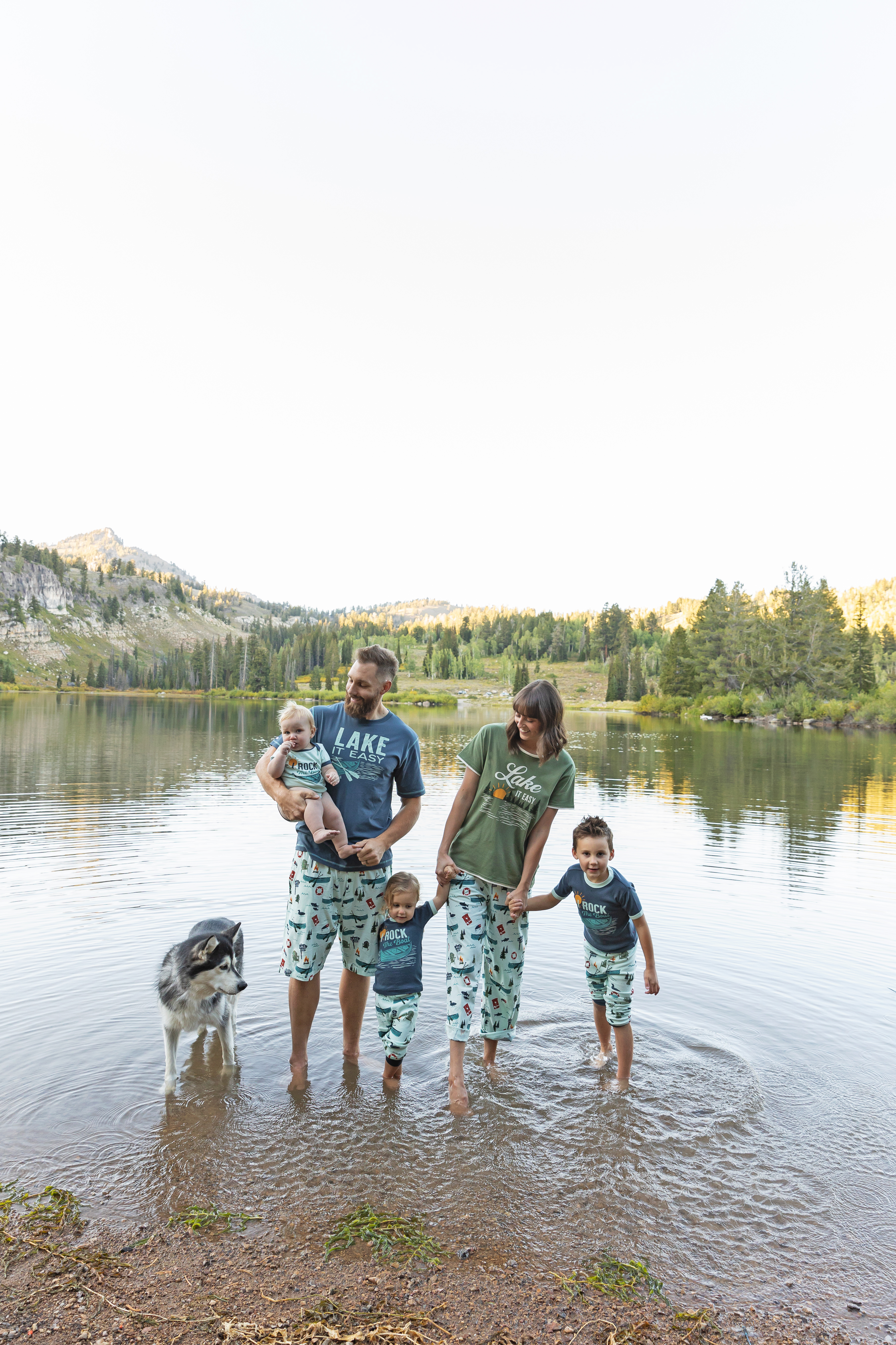 family of five wearing matching pajamas while standing ankle-deep in a lake with a large dog