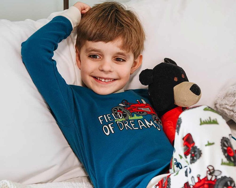 boy laying in bed with field of dreams tractor pajamas and stuffed bear