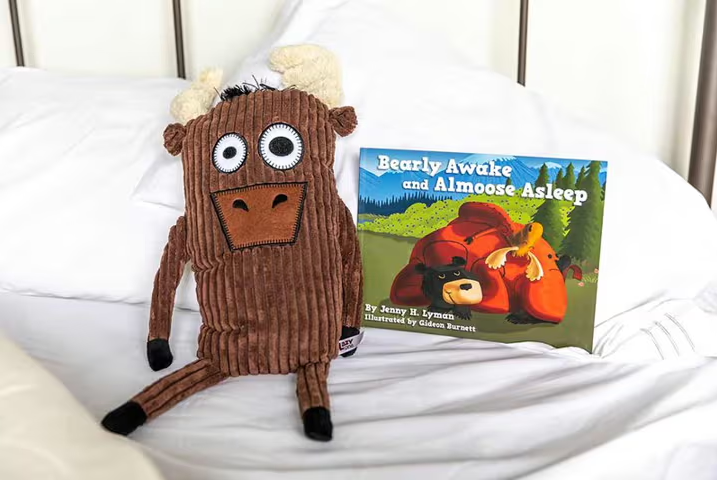 moose stuffed animal and kids storybook propped up on pillows in an unmade bed