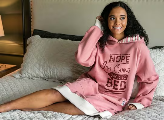 woman wearing a pink oversize sleep hoodie lounging on a full size bed