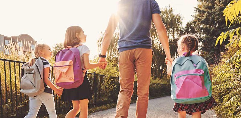 father and three girls with school backpacks holding hands walking down a trail